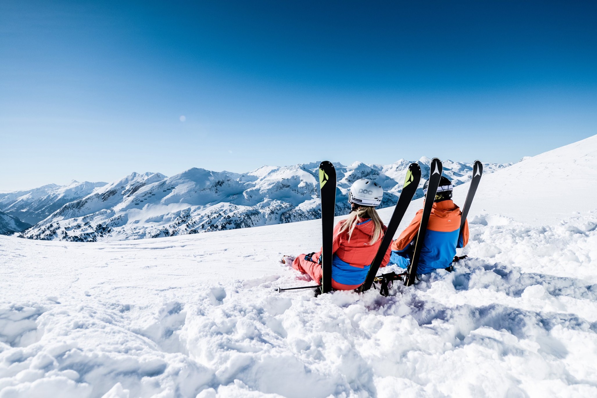 Zwei Skifahrer entspannen auf einem verschneiten Berg mit Blick auf die Berge Obertauerns. ©TVB_Obertauern