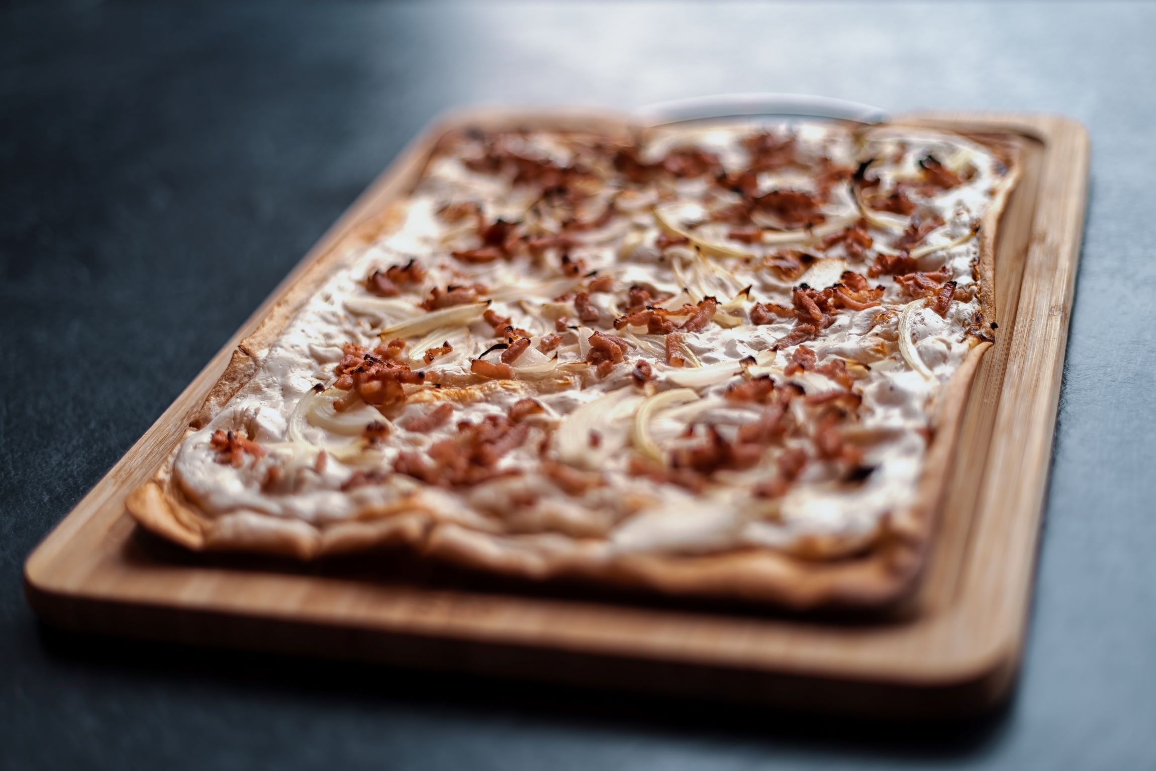 Detailaufnahme eines Flammkuchens mit Speck aus dem Restaurant Tauernstüberl vor schwarzem Hintergrund. © Shutterstock