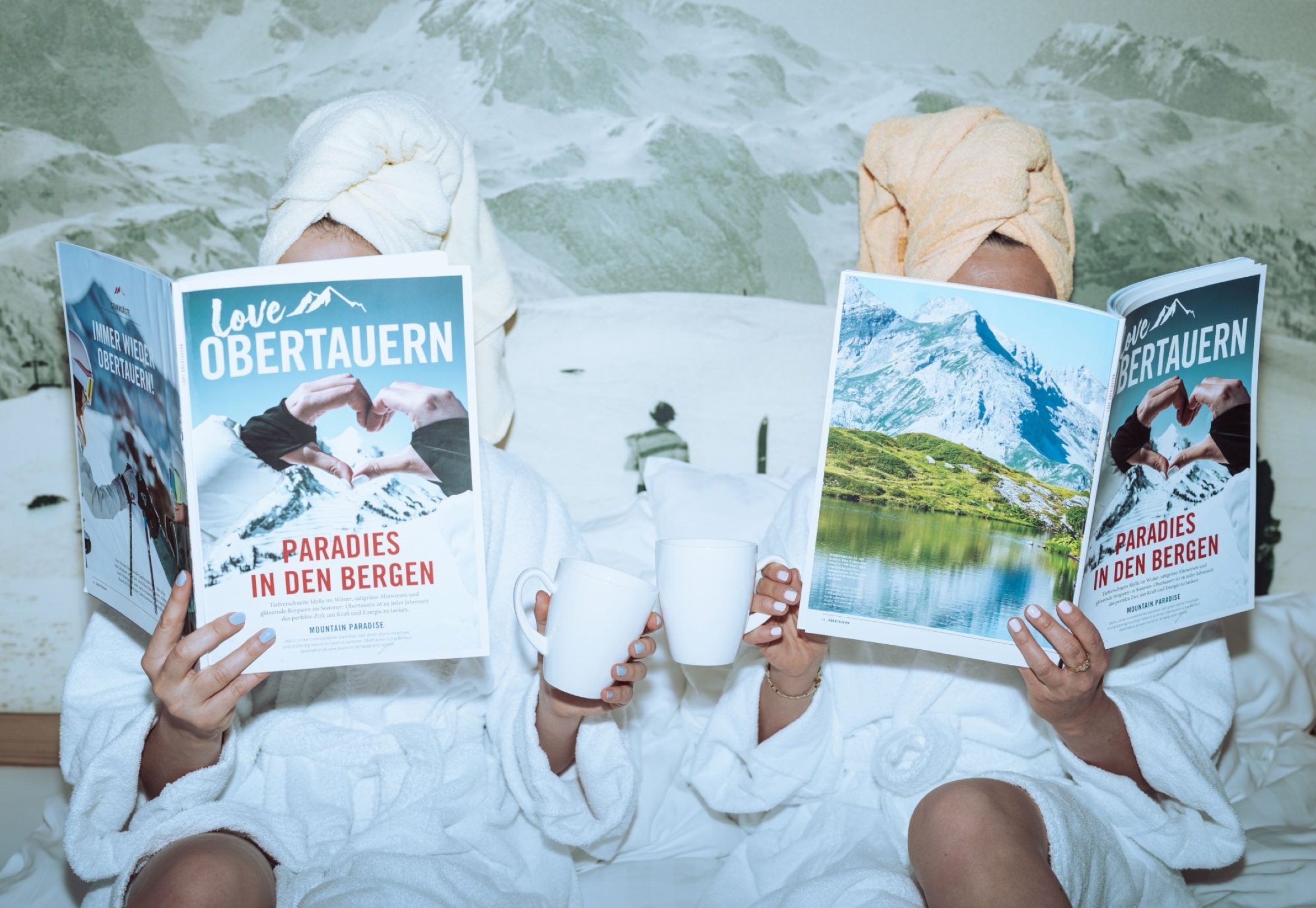 Zwei Gäste entspannen im Bett des Wagner Hotels in Obertauern mit einer Tasse Kaffee und lesen Magazine nach einem Tag im Schnee.