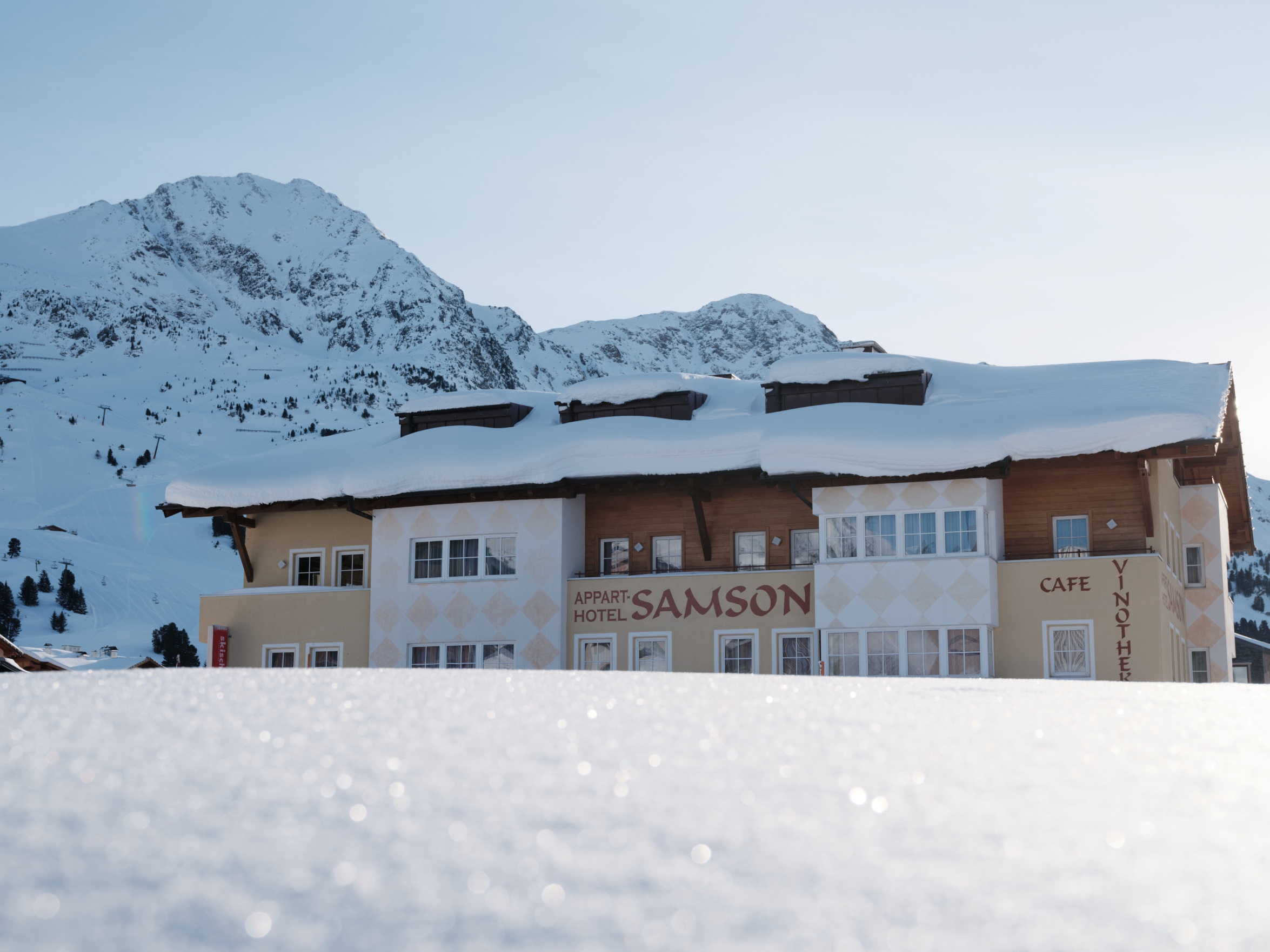 Außenansicht des Apparthotels Samson in Obertauern in bester Lage direkt an der Skipiste, umgeben von schneebedeckten Bergen.