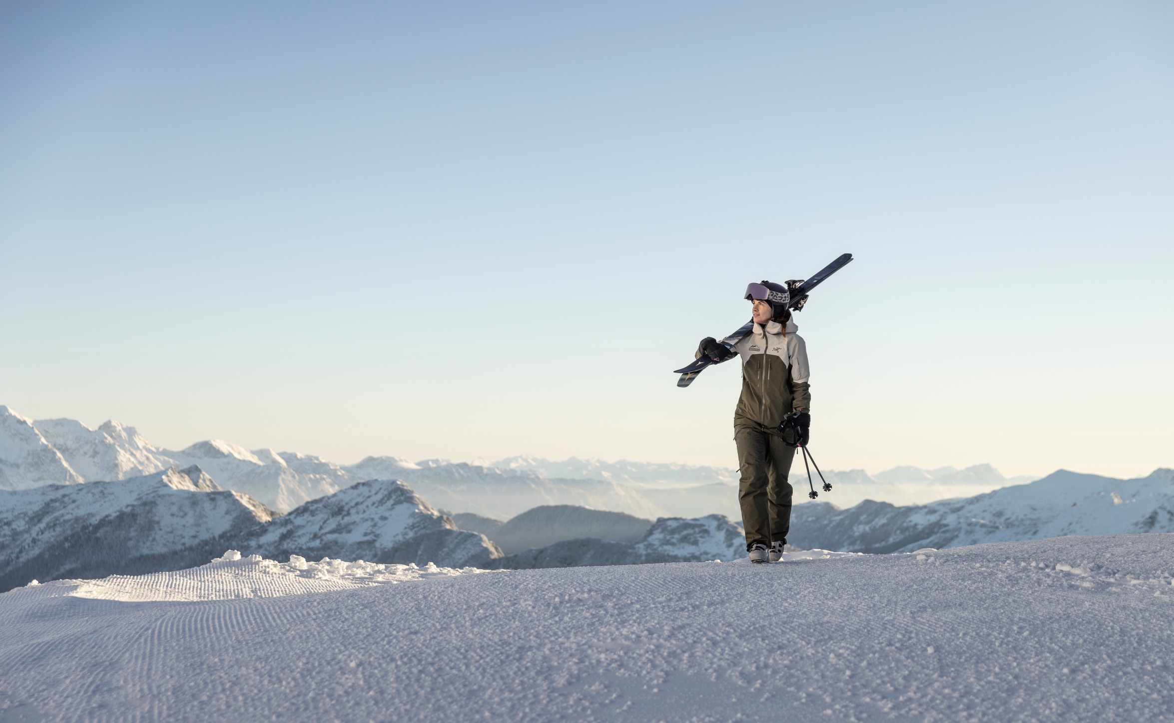 Skifahrerin mit geschulterten Skiern geht auf hohem beschneiten Berg und schaut auf die anderen Gipfel hinab. ©TVB_Obertauern