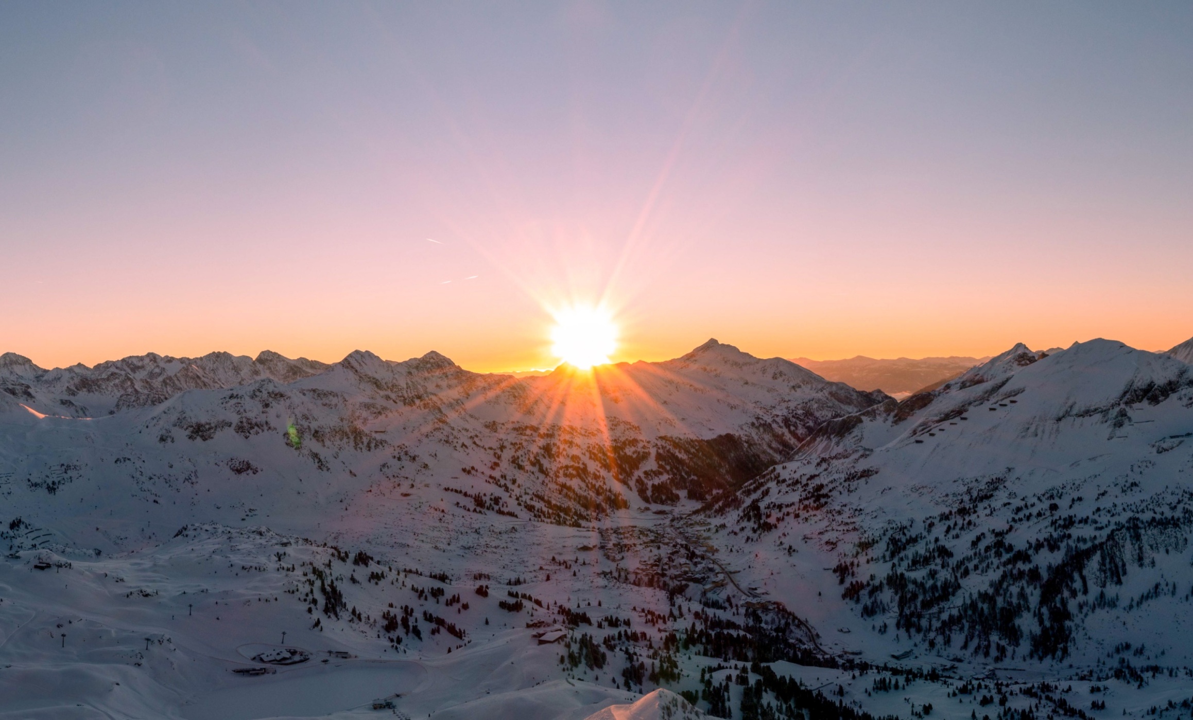 Schneebedeckte Berge unter einem rosa-orangefarbenen Himmel bei Sonnenaufgang