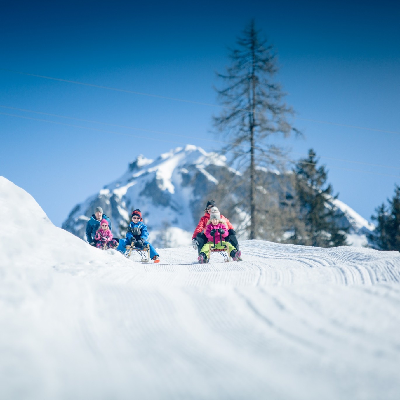 Familien fahren auf Schlitten einen verschneiten Hang in Obertauern hinunter ©TVB_Obertauern/Markus Rohrbacher