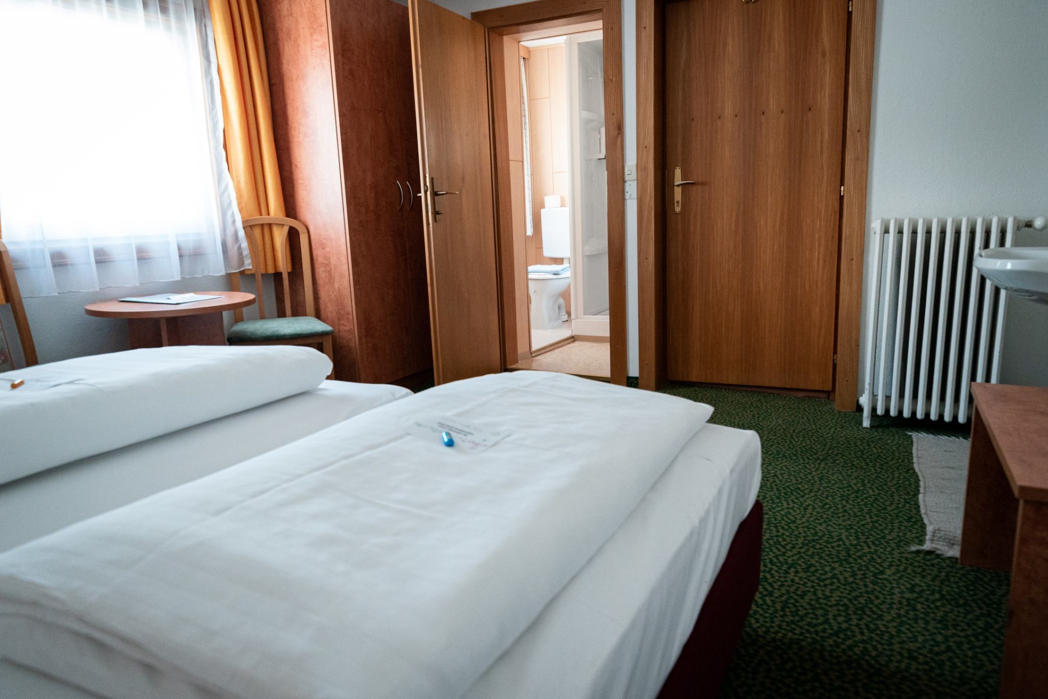 Doppelzimmer im Hotel Tauernpasshöhe mit grünem Teppich, Holzmöbeln und großem Fenster mit Tageslicht.