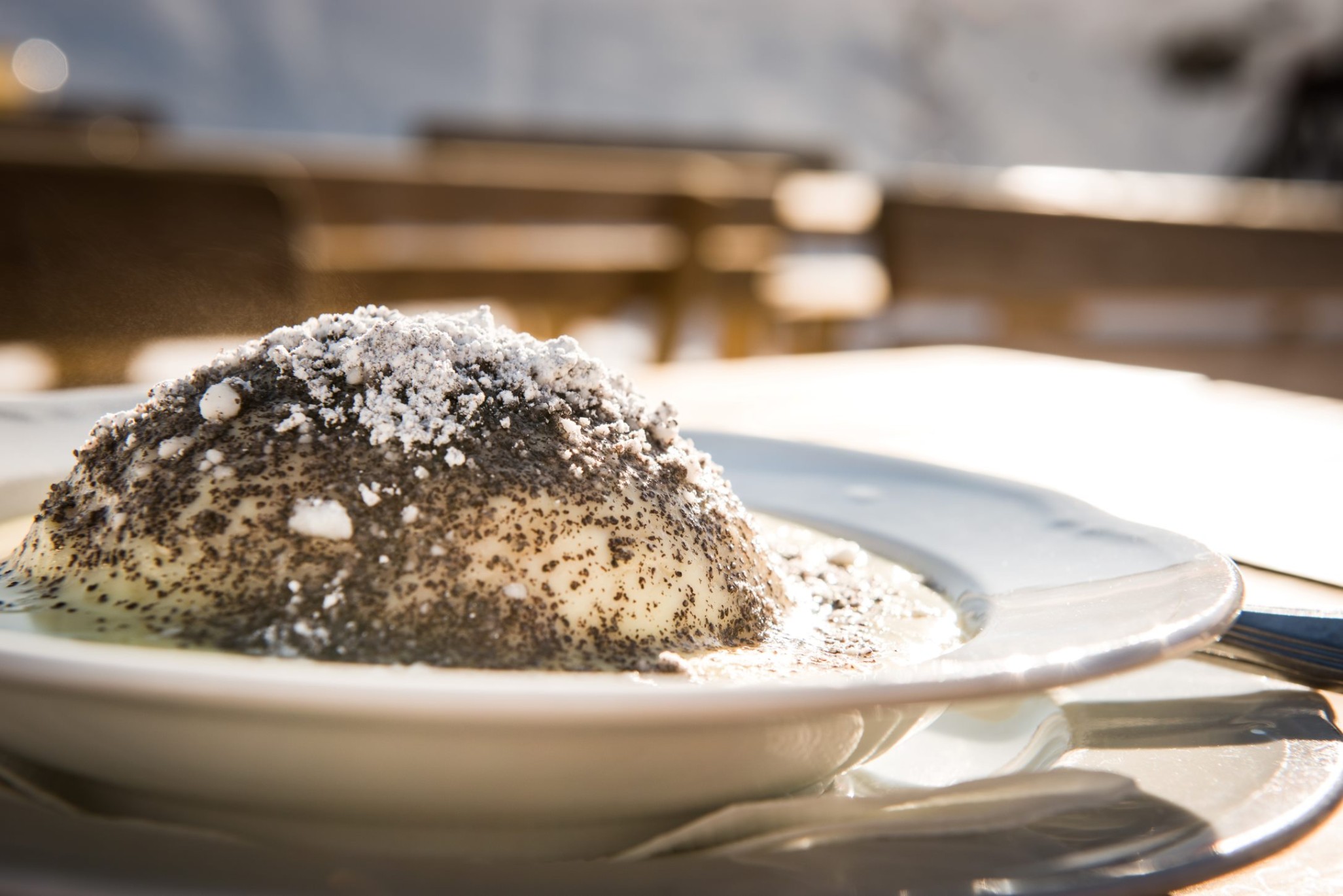 Ein Germknödel mit Mohn und Puderzucker auf einem Teller, draußen serviert ©TVB_Obertauern