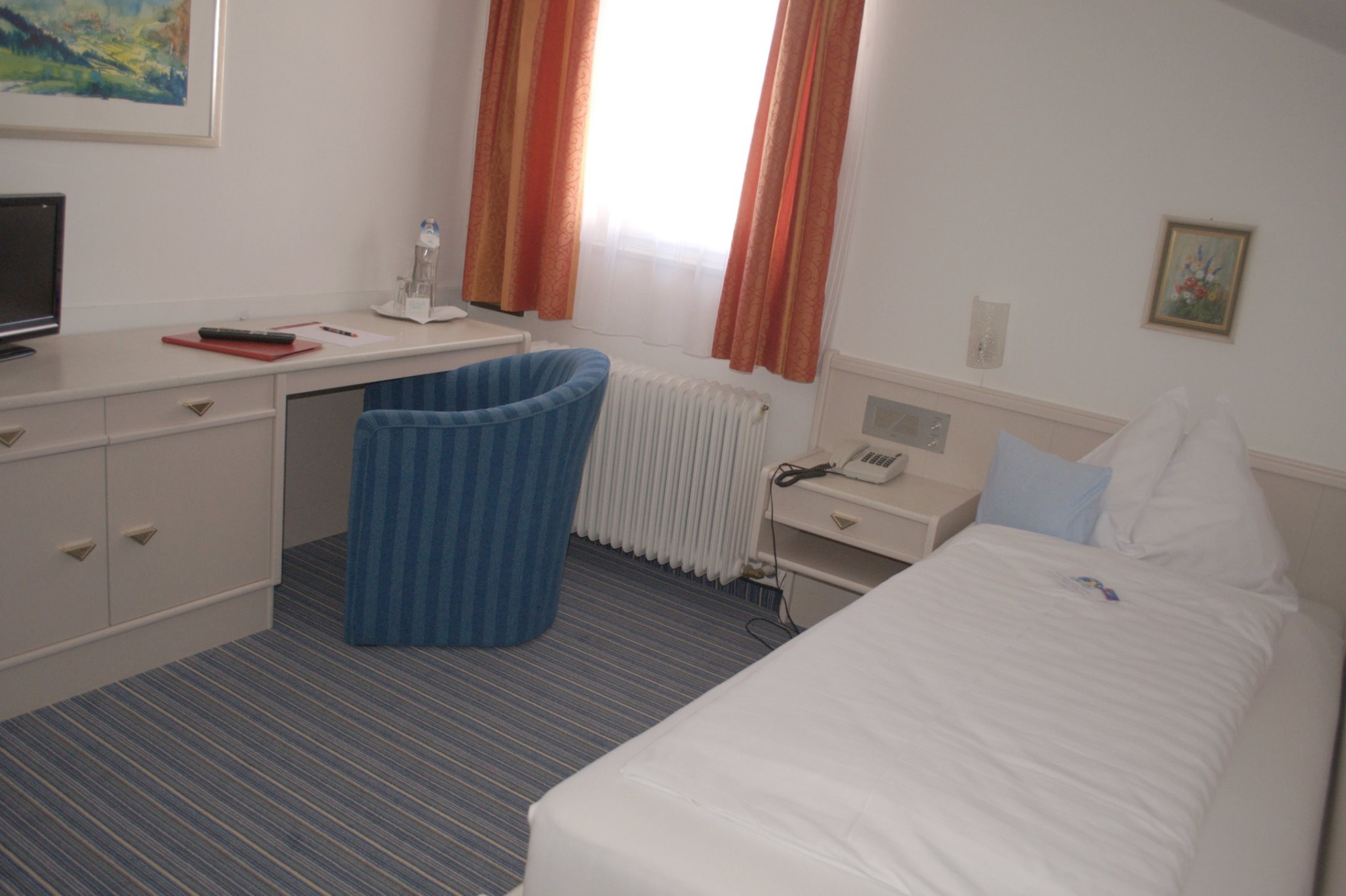 Ein einfaches Hotelzimmer mit Einzelbett, Schreibtisch, Stuhl und Fernseher