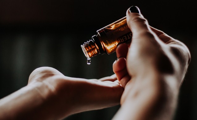 Eine Person träufelt Öl aus einer braunen Flasche auf ihre Hand